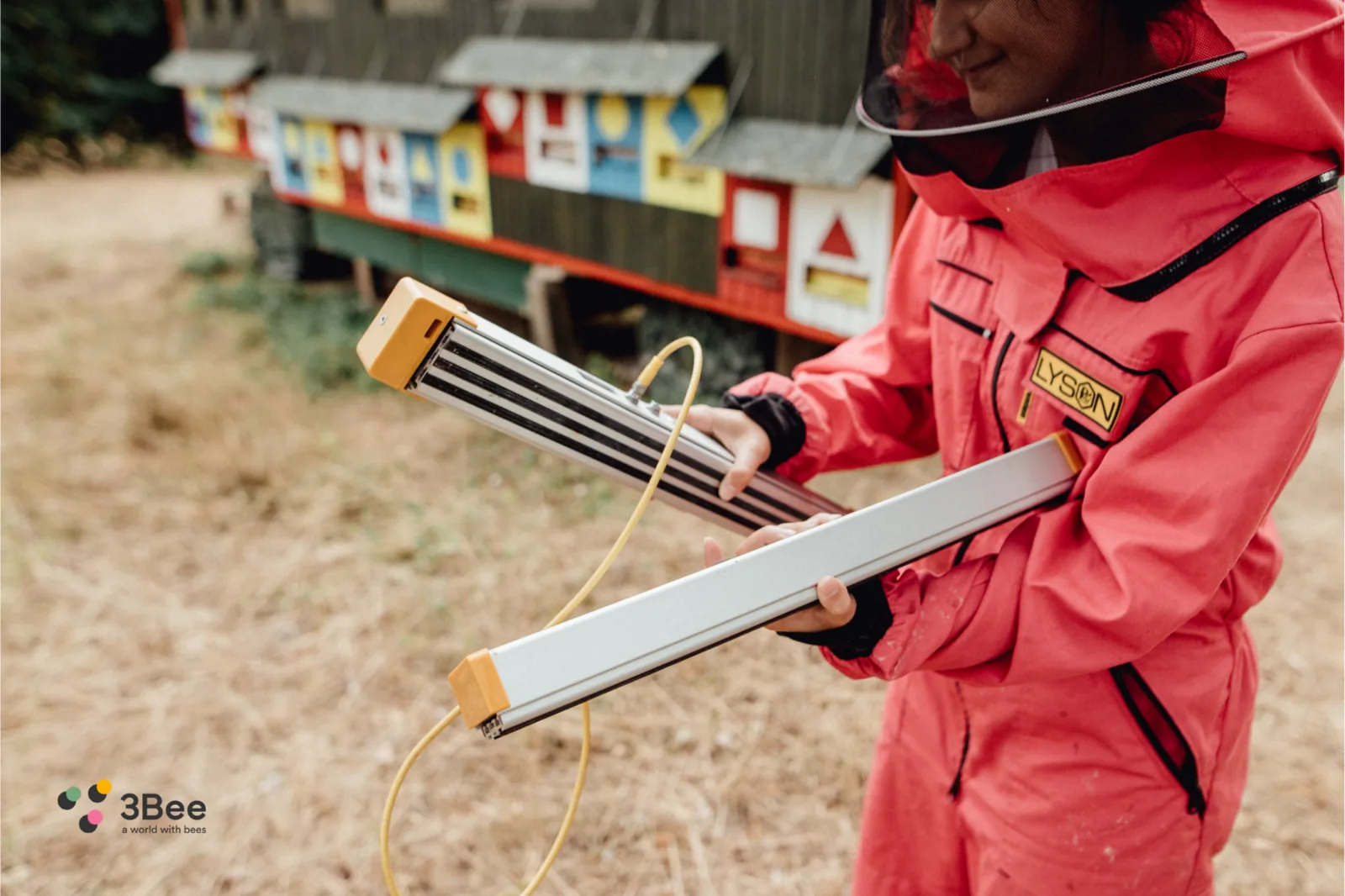 Apicoltrice con in mano le due barre della bilancia Hive-Tech davanti a un apiario